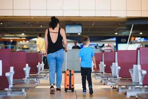 familj på flygplats innan flyg. mor och son väntar till styrelse på avresa Port av modern internationell terminal. reser och flygande med barn. mamma med unge ombordstigning flygplan. gul familj foto