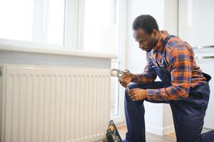 reparera uppvärmning radiator närbild. afrikansk man reparation radiator med rycka. avlägsnande luft från de radiator foto