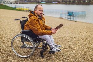 paraplegic handikappade man i rullstol är läsning bok utomhus. foto