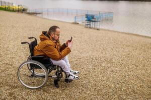 paraplegic handikappade man i rullstol är meddelandehantering på smartphone utomhus. foto