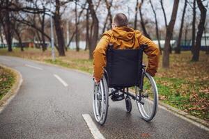 bak- se bild av paraplegic handikappade man i rullstol i parkera. han är rullande på väg. foto