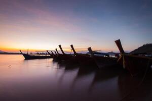 lång svans båt på tropisk strand, under molnig himmel foto