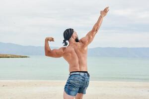 ung muskulös man utövar på de strand, ung muskulös man håller på med kroppsbyggnad övningar på de strand, atletisk ung man på de strand foto