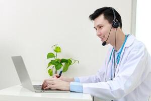 asiatisk manlig läkare leende vackert tillhandahålla behandling tjänster för patienter med uppkopplad samtal via de internet på bärbar dator datorer. uppkopplad läkare begrepp. kopia Plats foto