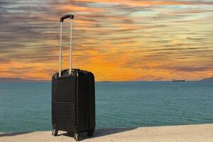 en resväska är stående på en strand med en solnedgång i de bakgrund. resa, Semester och semester koncept. sommar tid. foto