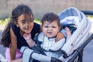 en små syster med henne bebis pojke bror i en rullstol foto