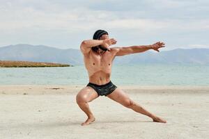 ung muskulös man utövar på de strand, ung muskulös man håller på med kroppsbyggnad övningar på de strand, atletisk ung man på de strand foto