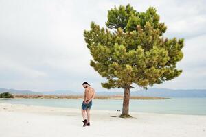 ung muskulös man utövar på de strand, ung muskulös man håller på med kroppsbyggnad övningar på de strand, atletisk ung man på de strand foto