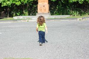 Lycklig liten pojke spelar i de parkera, lång hår pojke i de parkera foto