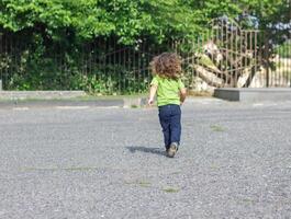 Lycklig liten pojke spelar i de parkera, lång hår pojke i de parkera foto