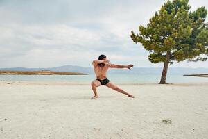 ung muskulös man utövar på de strand, ung muskulös man håller på med kroppsbyggnad övningar på de strand, atletisk ung man på de strand foto