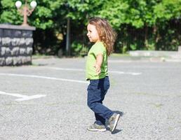 Lycklig liten pojke spelar i de parkera, lång hår pojke i de parkera foto