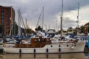 marina med olika segelbåtar och yachter dockad på en molnig dag, med byggnader i de bakgrund. foto