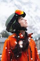 leende ung kvinna, porträtt, stående och njuter snöfall, bär skyddande Kläder, hjälm och glasögon. vinter- sporter tillflykt foto
