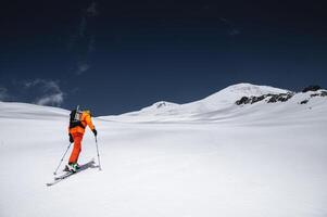 en skidåkare i ett orange kostym skidor i en berg offpist skidåkning i de nordlig kaukasus av montera elbrus foto