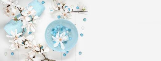 turkos skål med vatten och mor av pärla spa stenar för mild manikyr i de salong med vit magnolia blommor foto