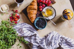 frukost med kaffe, croissanter, bär, honung och Smör foto