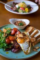 frukost med friterad ägg, bacon, skålar och vegetabiliska sallad foto