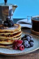 pannkakor med bär och en kopp av kaffe på en trä- tabell foto