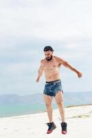 ung muskulös man utövar på de strand, ung muskulös man håller på med kroppsbyggnad övningar på de strand, atletisk ung man på de strand foto