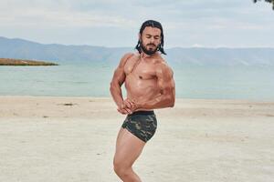 ung muskulös man utövar på de strand, ung muskulös man håller på med kroppsbyggnad övningar på de strand, atletisk ung man på de strand foto