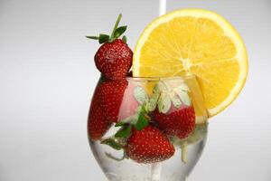 en glas av vatten med jordgubbar och ett orange skiva foto