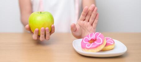kvinna hand håll grön äpple och avvisa munk, kvinna kondition välja mellan frukt är friska och ljuv är ohälsosam skräp mat. bantning kontrollera, vikt förlust, fetma, äter livsstil och näring foto
