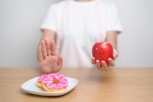 kvinna hand håll röd äpple och avvisa munk, kvinna kondition välja mellan frukt är friska och ljuv är ohälsosam skräp mat. bantning kontrollera, vikt förlust, fetma, äter livsstil och näring foto
