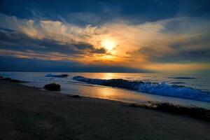 solnedgång, upplyst hav. sandig strand i de förgrund. ljus vågor. baltic hav foto