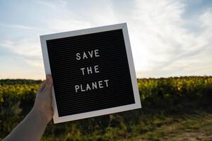 oigenkännlig person med baner meddelande spara de planet i solros fält på solig dag. tecken jord dag. begrepp av ekologi och eco aktivism miljö- frågor sluta global uppvärmning. gå grön hållbar foto