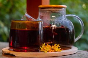 calendula blomma friska te i glas råna med te pott på trädgård tabell. ört- medicin utsökt kisligt te med färsk gul blomma maskros blommor te kopp. grön clearing infusion vild eco vänlig hållbar äter foto