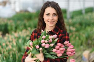 skön ung leende flicka, arbetstagare med blommor i växthus. begrepp arbete i de växthus, blommor. foto