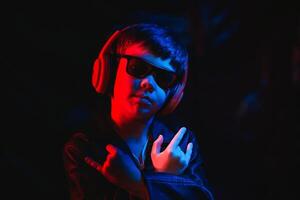studio skott i mörk studio med neon ljus. porträtt av en eleganta pojke med hörlurar foto