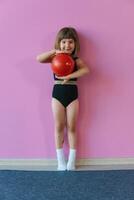 flicka gymnast i en eleganta trikåer Framställ med en röd gymnastiska boll. skön flicka idrottare. sporter i barndom foto