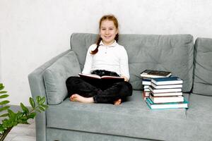 leende Söt flicka på de soffa omgiven förbi böcker foto