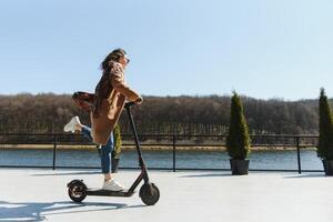 ung skön kvinna ridning ett elektrisk skoter till arbete, modern flicka, ny generation, elektrisk transport, ekologi, ekologisk transport, solnedgång, elektrisk skateboard. foto