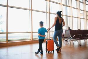 familj på flygplats innan flyg. mor och son väntar till styrelse på avresa Port av modern internationell terminal. reser och flygande med barn. mamma med bebis och litet barn ombordstigning flygplan. foto