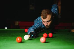 ung stilig man lutande över de tabell medan spelar snooker foto