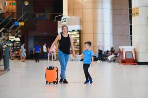 familj på flygplats innan flyg. mor och son väntar till styrelse på avresa Port av modern internationell terminal. reser och flygande med barn. mamma med unge ombordstigning flygplan. gul familj foto