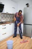 professionell rengöringsmedel i blå enhetlig tvättning golv och avtorkning damm från de möbel i de levande rum av de lägenhet. rengöring service begrepp foto