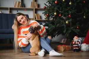 skön kvinna sitter på en årgång soffa med hund. på en bakgrund av en jul träd i en dekorerad rum. Lycklig ny år foto