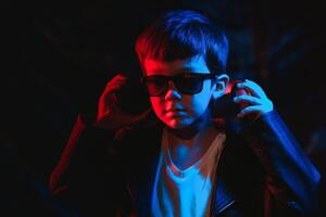 studio skott i mörk studio med neon ljus. porträtt av en eleganta pojke med hörlurar foto