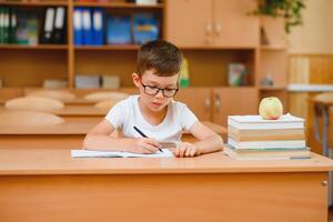 elementärt skola pojke på klassrum skrivbord påfrestande till hitta ny idéer för skolarbete. foto