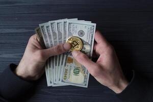 gyllene bitcoin och dollar i manlig hand på en mörk blå trä- bakgrund. guld mynt av kryptovaluta. foto