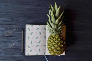 ananas och anteckningsbok på de mörk blå trä- tabell. abstrakt eleganta bakgrund. foto