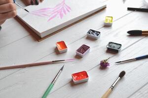 kvinna målarfärger i en skissbok. verktyg för målning på de vit trä- skrivbord. målare arbete. foto