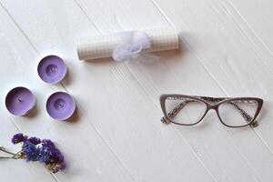 brev, glasögon, ljus och blomma på de vit tabell. vacker kvinna objekt på de vit trä- bakgrund. platt lägga i violett Färg. foto