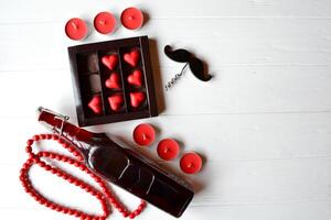 de låda med godis i en form av hjärta. röd godis, vin och röd ljus på de vit trä- tabell. bakgrund för hälsning kort på hjärtans dag. foto