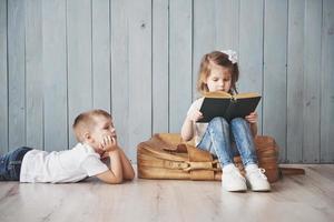 redo för stora resor. glad liten flicka och pojke som läser intressant bok som bär en stor portfölj. frihet och fantasi koncept foto