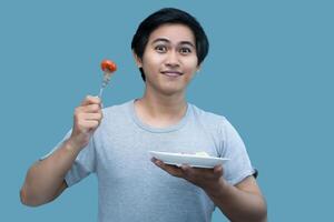 en man i en grå skjorta är innehav en gaffel och en tallrik som innehåller mat, för design och visuell redigering syften. foto